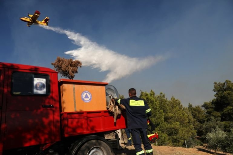 A firefighting aircraft flies over a fire engine during efforts to contain a wildfire near Pikermi suburb, east of Athens, Greece, 03 July 2025. 