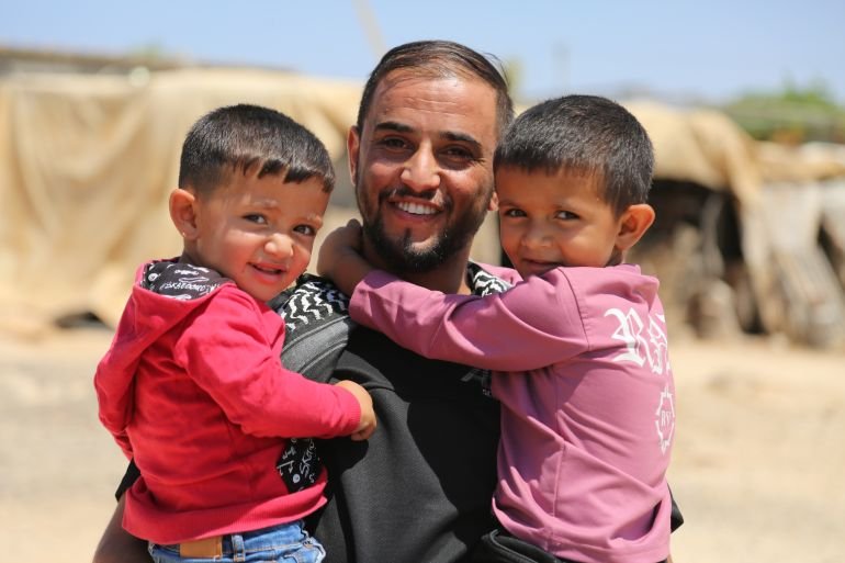 Two cute boys cling to their uncle's neck and look at the camera.