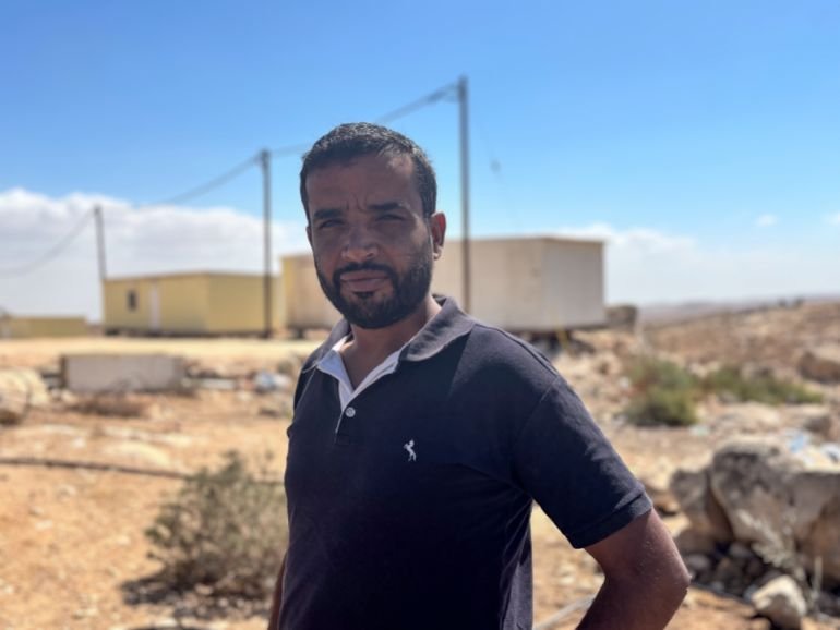Khalil Al-Hathaleen, a gentle-looking man squinting in the bright sun, with the Israeli caravans blurred in the background