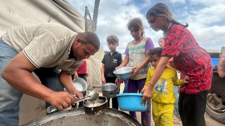 Tawfiq al-Najili handing out food from a pot to children