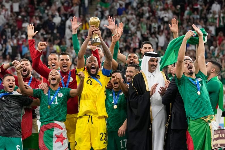 Algeria goalkeeper Rais Mbolhi holds up the winner trophy after received it from Qatar's Emir Sheikh Tamim bin Hamad Al Thani, second right, and FIFA President Gianni Infantino end of the Arab Cup final soccer match between Tunisia and Algeria at the Al Bayt stadium in Al Khor, Qatar, Saturday, Dec. 18, 2021. Algeria won 2-0. (AP Photo/Darko Bandic)