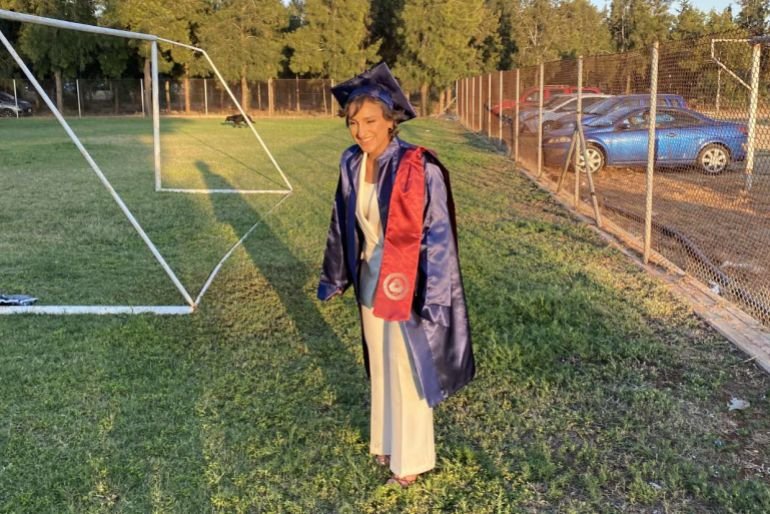 Young woman in cap and gown on a football pitch