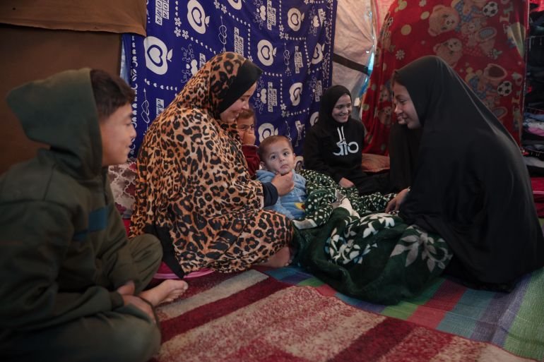 Sana’a sits with her children inside their tent, holding on to hope that living conditions will improve in the coming year [Abdelhakim Abu Riash/ media]