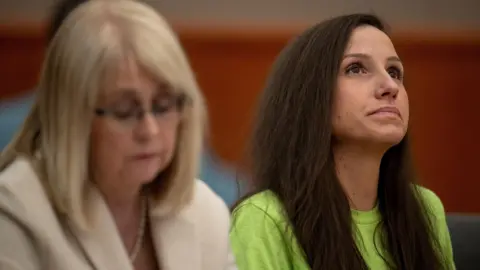 Reuters Kouri Richins in neon green T-shirt with long brown hair tilts her face and looks up while frowning slightly