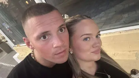 Lexie McGaughey Lexie and Evan, a young couple in a selfie. They are both wearing black. Evan has short fair hair and Lexie has long blonde hair