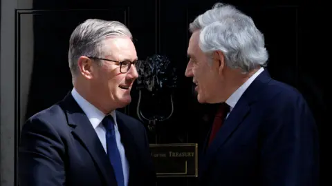 X/Keir Starmer Keir Starmer, wearing glasses and a blue suit and tie, is seen side on shaking hands with Gordon Brown, who is in a blue suit and red tie, outside No 10
