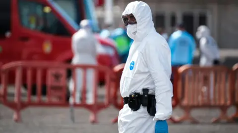 Reuters An officer wearing protective medical garments is seen during the disembarkation of passengers from the MV Hondius cruise ship