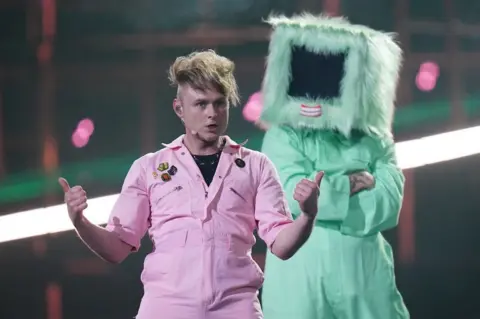 EPA Look Mum No Computer in a pink boiler suit with a dancer in a green one and a fluffy box on their head behind him