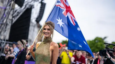 Getty Images Delta Goodrem in a gold, sleeveless dress carrying the Australian flag