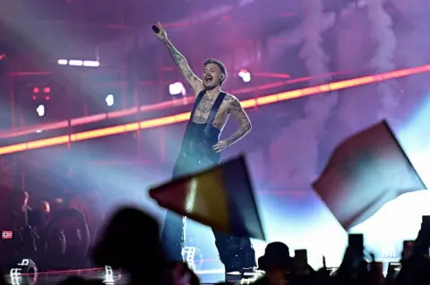 Getty Images Jonas Lovv in blue trousers and braces with no top on, performing on stage