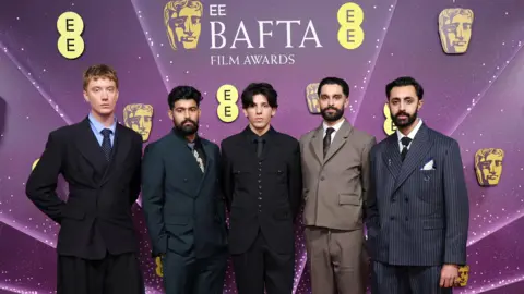 Getty Images Aidan Robert Brooks, Sufiyaan Salam, Luís Hindman, Eben Figueiredo and Gurjeet Singh in suits in a row in front of a Bafta Film Awards-branded backdrop