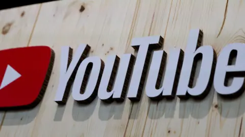 EPA The YouTube logo, in white writing beside the play button symbol of a white triangle on a red background, placed on light wooden boards.