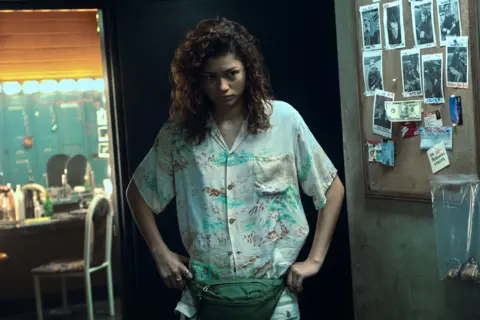 Eddy Chen/HBO Zendaya as Rue wearing a white shirt and hands on her hips 