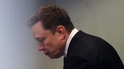 Reuters Elon Musk wearing a black suit jacket, matching neck tie and white dress shirt, going through a security check at an Okaland, California courthouse