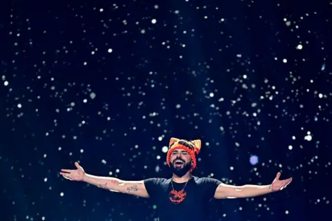 Getty Images Akylas in a black T shirt and an orange hat with ears with his arms outstretched