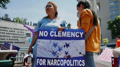 KENA BETANCUR/AFP via Getty Images Demonstrators gathered outside the Manhattan federal court after the sentencing of former Honduran President Juan Orlando Hernandez Alvarado in June 2024 in New York, hold up a sign reading "no clemency for narcopolitics".