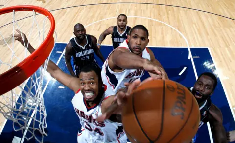Kevin C. Cox / Getty Images Jason Collins of the Atlanta Hawks reaches for the ball alongside another player, while attempting a rebound into the net, with players on the other team looking on in the background, against the Orlando Magic in 2011.