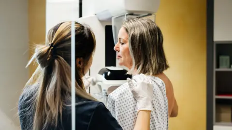 Getty Images A nurse provides assistance to a patient undergoing a mammogram in a modern medical facility. 