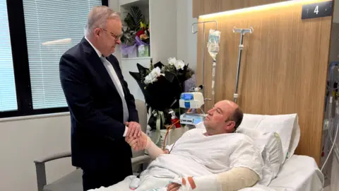 Reuters A man in a dark suit shakes the hand of a man lying in a hospital bed