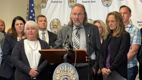 Submitted photo Wearing a grey suit and tie, Krug's father speaks at a podium, on his right is his wife, Kristil's stepmother and on his left, Kristil's mum, Linda Grimsrud