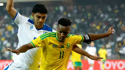 AFP via Getty Images A South Africa player holds his arms out as he tries to stop a Nicaraguan player from coming up form behind him.