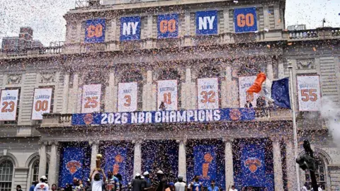 REUTERS/Dylan Martinez General view as New York Knicks' Jalen Brunson and Trey Jemison III hold the Larry O'Brien Championship Trophy and the NBA Cup at New York City Hall during the parade 