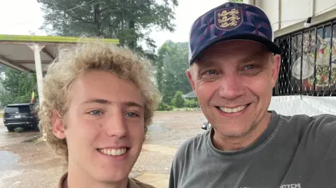 Iain Bagwell Iain Bagwell, right, is a man in his 50s. He takes a selfie with his teenage son, pictured left. Both smile for the camera.