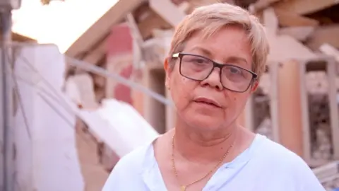 BBC Zuly Marín, dressed in a white shirt and black glasses, stares into space.