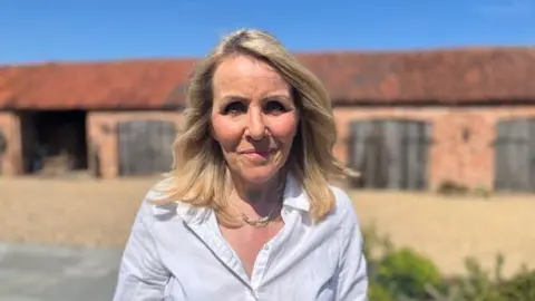 Sue Brydon, wearing a necklace and white shirt, poses for a photo outside her home.