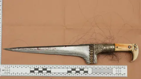 Crown Prosecution Service A silver dagger is pictured from above. Its handle it ivory in colour. Below the blade, which is pointing to the left, is a ruler measuring its length.