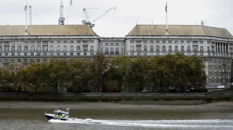 Reuters The image shows a huge grey office block shown on the banks of the River Thames, with a police boat in the foreground in the water
