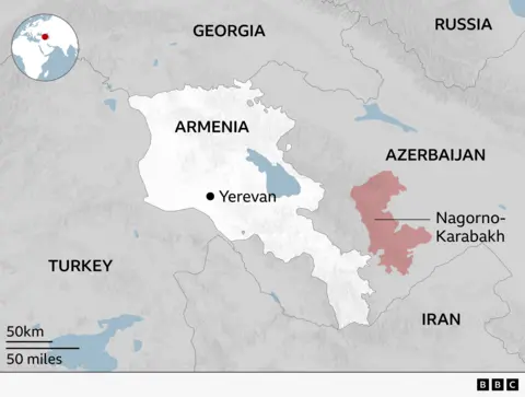 Map of the South Caucasus highlighting Armenia in white with its capital Yerevan marked by a black dot. Surrounding countries are labelled: Turkey to the west, Georgia to the north, Azerbaijan to the east, and Iran to the south, with Russia shown further northeast. The region of Nagorno-Karabakh is shaded in red within Azerbaijan to the east of Armenia. A small inset globe in the top-left shows the region’s location in the world, and a scale bar indicates distances of 50 km and 50 miles.

