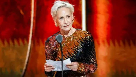 Getty Images Laurie Metcalf at The 79th Annual Tony Awards, accepeting her acting prize while wearing an orange, black and brown sequined dress