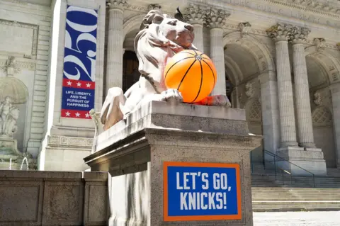 Courtesy of the New York Public Library The lion statue named Patience that stands outside the New York Public Library's 5th Avenue branch is now decorated with an inflatable basketball.