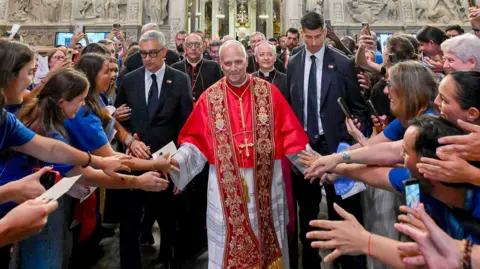 Getty Images Pope Leo XIV is dressed in an ornate red habit and is reaching out to crowds, smiling. 