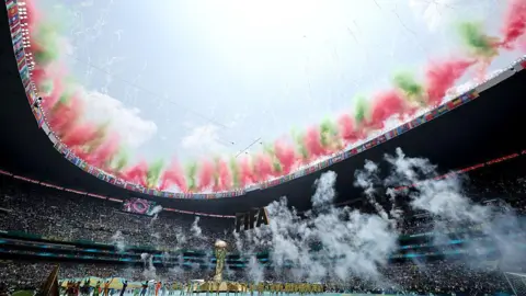 Getty Images Fireworks display in the colours of the Mexican flag light up the edge of the open stadium roof during the Opening Ceremony. A massive golden mock World Cup trophy is on the pitch. 