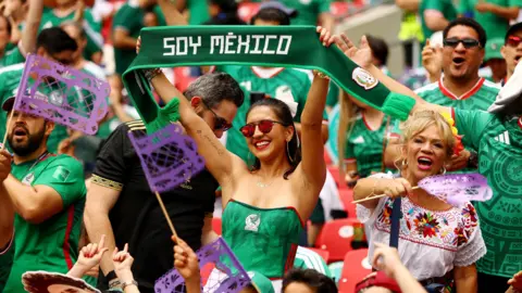 Reuters Mexico fans, dressed in green jerseys, smile and wave signs and flags inside the stadium before the match 