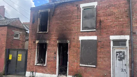 A red-bricked house has been burnt out/boarded up.