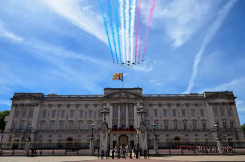 Reuters The Red Arrow take part in the flypast over Buckingham Palace. Twelve aircraft are pictured with plumes of red, white and blue clouds in their wake through a blue sky.