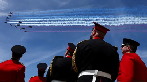 Reuters Members of the British military in ceremonial uniforms watch the Red Arrows perform a flypast