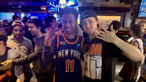 Grace Eliza Goodwin/BBC two men wearing Knicks jerseys smiling and holding up their hands in a "5" signal
