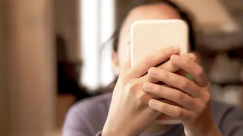 Getty Images A young girl hold a smartphone in front of her face. Her face cannot be seen.