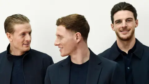 Marks & Spencer Jordan Pickford, Elliot Anderson and Declan Rice wearing dark jackets and standing against a white background 
