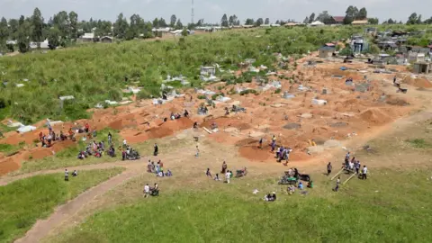 Amensisa Ifa / BBC An aerial view of a graveyard in Bunia showing lots of fresh graves and groups attending burials