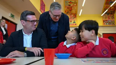 Getty Images Sir Keir Starmer looks over the shoulder of Andy Burnham as they chat to two children in school uniform on a visit to a breakfast club in Ashton-under-Lyne, Greater Manchester, in April.