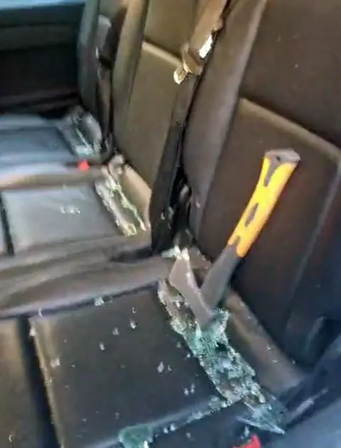 A yellow handled hand axe and broken glass on a vehicle seat