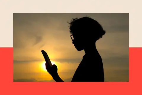 EPA A silhouette of a child looking at his mobile phone. He has shoulder-length hair and is wearing glasses. The Sun is shining behind him.