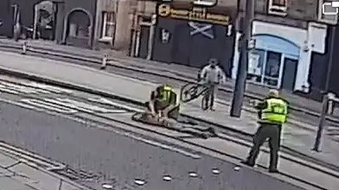 A man is lying on the ground being restrained by police officers in a street