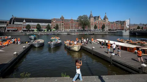 Getty Images A woman walks past a canal in the Netherlands, where crowds of people are getting onto boats