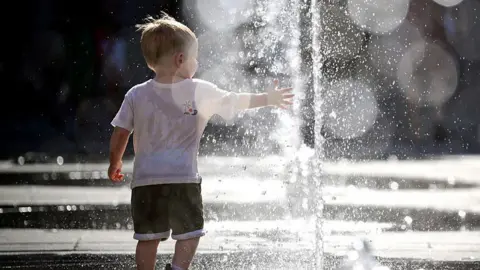 AFP via Getty Images A child, in a white T-shirt and black shorts, plays in a fountain during a heatwave in Lyon, south-eastern France on 18 June 2026